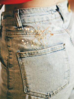 Close-up of denim jeans with delicate white flowers in back pocket, showcasing a stylish look.