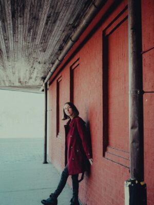 Stylish woman in a red coat poses by a rustic urban wall. Perfect for fashion and street photography.