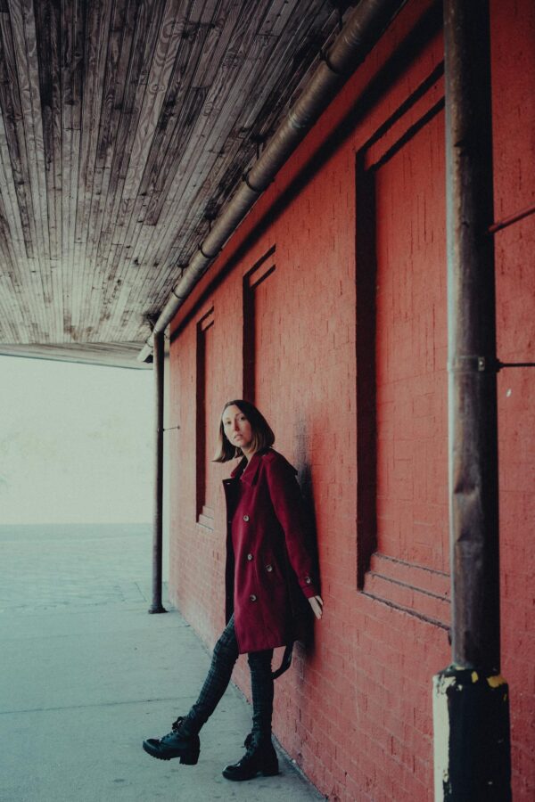 Stylish woman in a red coat poses by a rustic urban wall. Perfect for fashion and street photography.