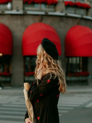 Stylish woman in black dress with red hearts holding a baguette on a street with red awnings.