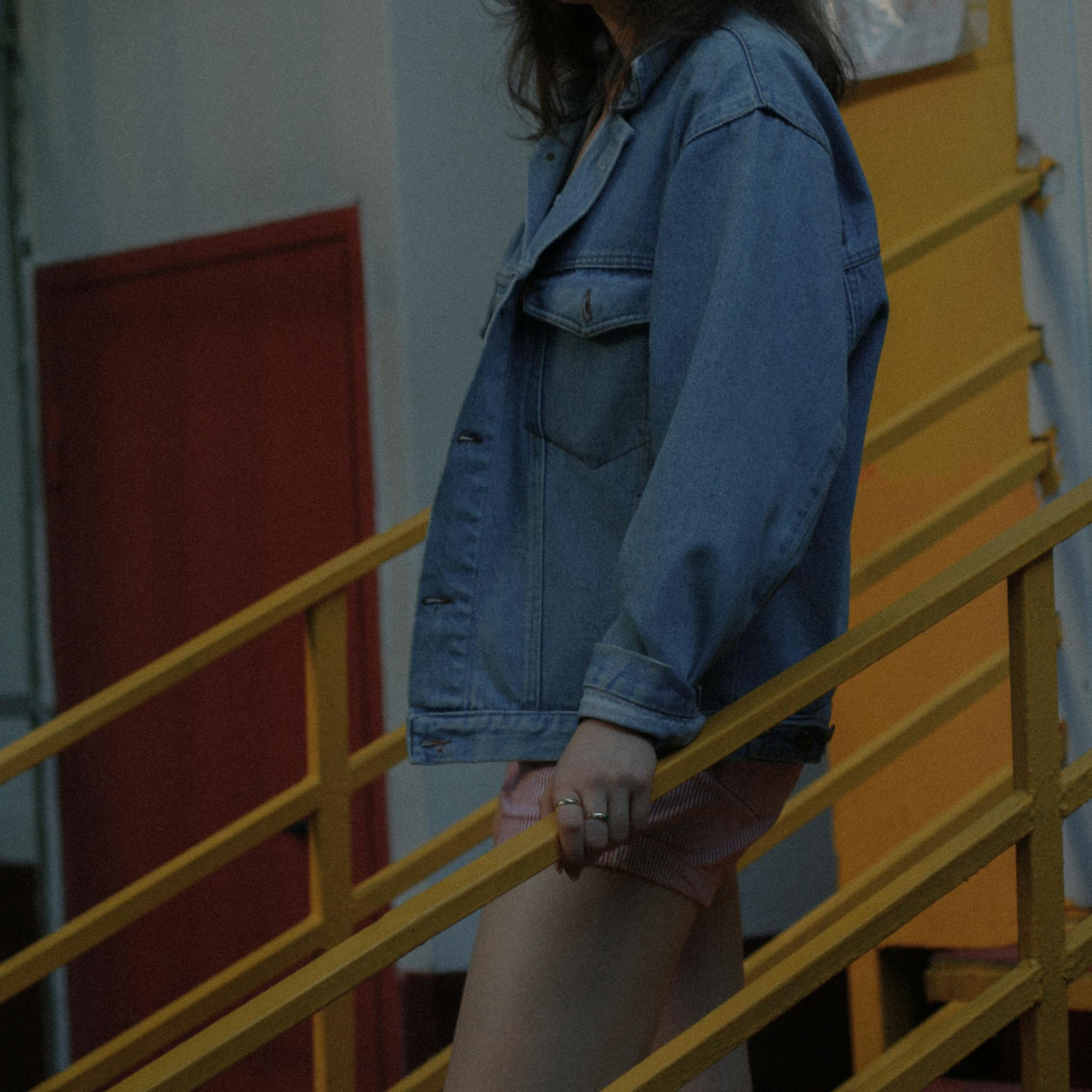 Stylish woman in denim jacket and shorts leaning on yellow handrails.